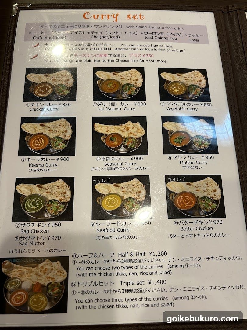 A printed menu featuring a variety of curry dishes with prices in yen, including Chicken Curry, Dal (Beans) Curry, Vegetable Curry, Keema Curry, Seasonal Curry, Mutton Curry, Sag Chicken, Seafood Curry, Butter Chicken, and Half & Half set options.