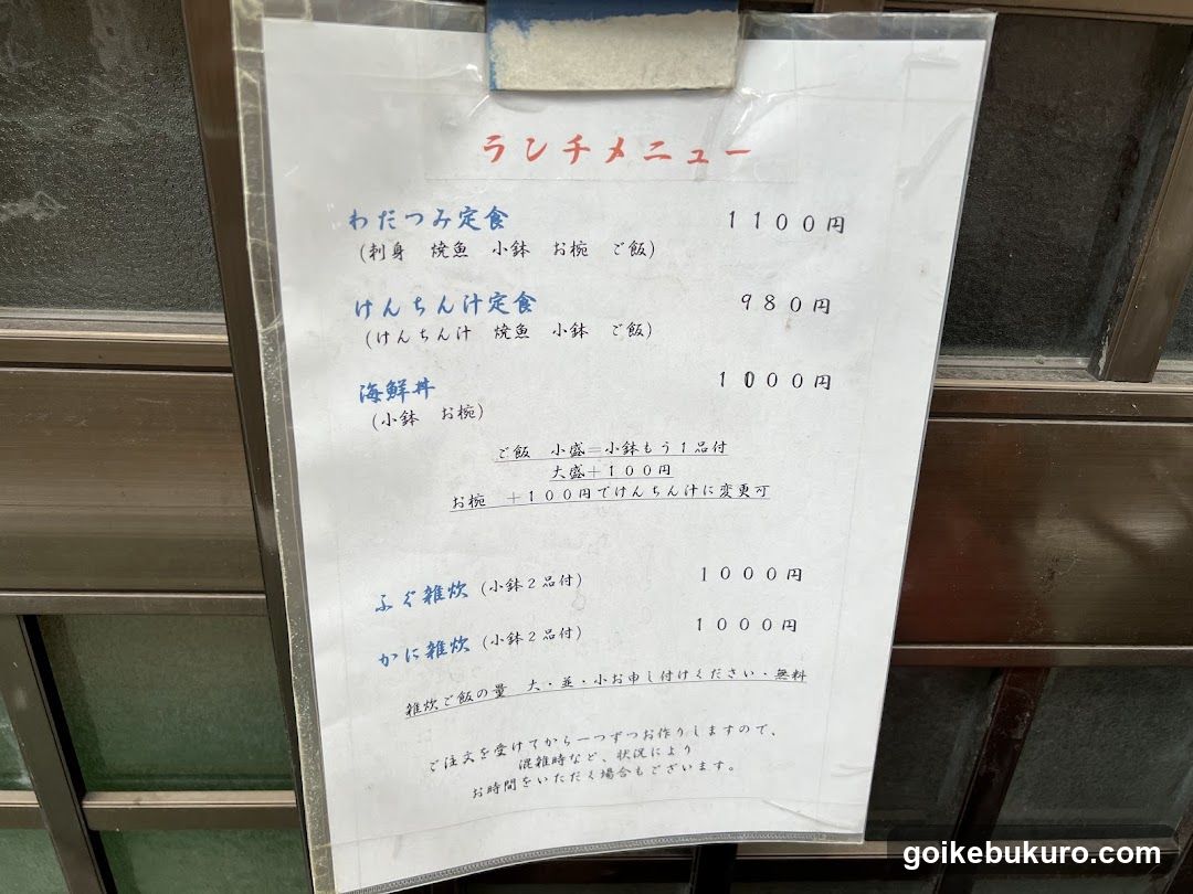 A laminated menu board attached to a glass door or window, listing lunch set meals and drinks with prices in yen.