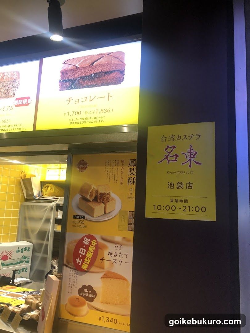 Storefront of Taiwan Castella Ichikado at Ikebukuro, featuring illuminated signage with product images and prices. Visible items include chocolate cake (¥1,700), cheese cake (¥1,340), and seasonal limited-time products like 'Tobiko' and 'Sunrise'. A yellow sign indicates operating hours from 10:00 to 21:00.