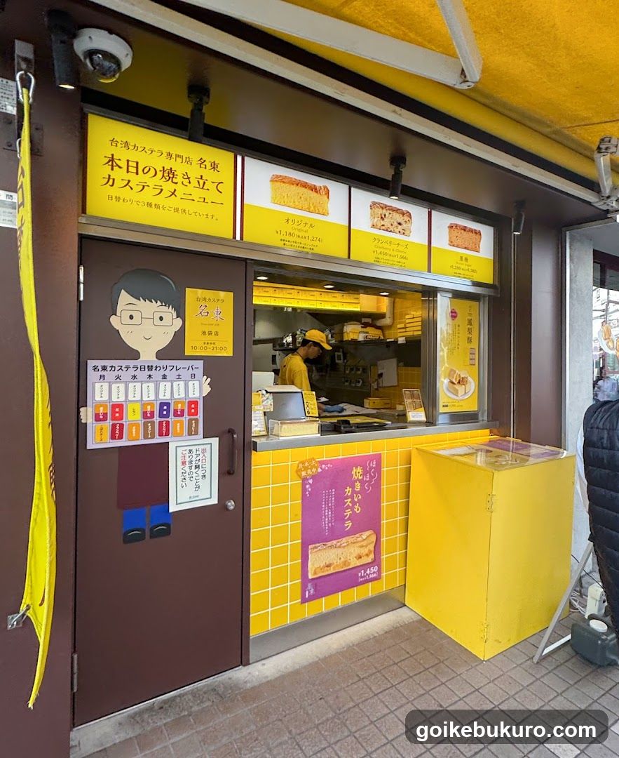 A storefront with yellow and brown exterior, featuring a menu board above the entrance displaying caramel products like 'Orange' and 'Strawberry'. A cartoon character sticker is on the door, along with a schedule poster. Inside, staff in yellow uniforms are visible behind the counter.