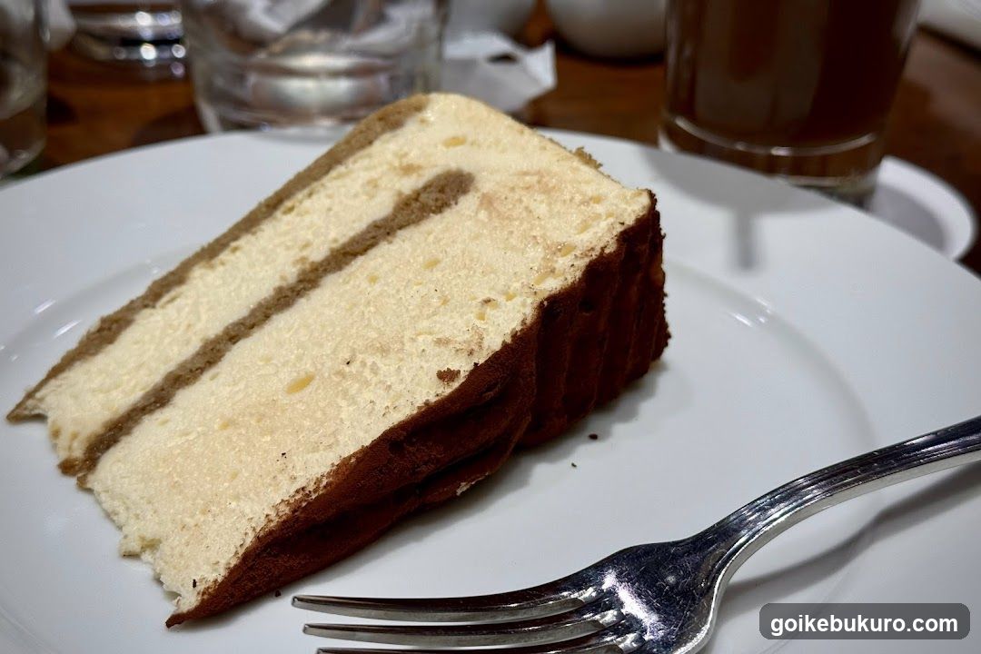 Slice of layered cake on a white plate with fork nearby