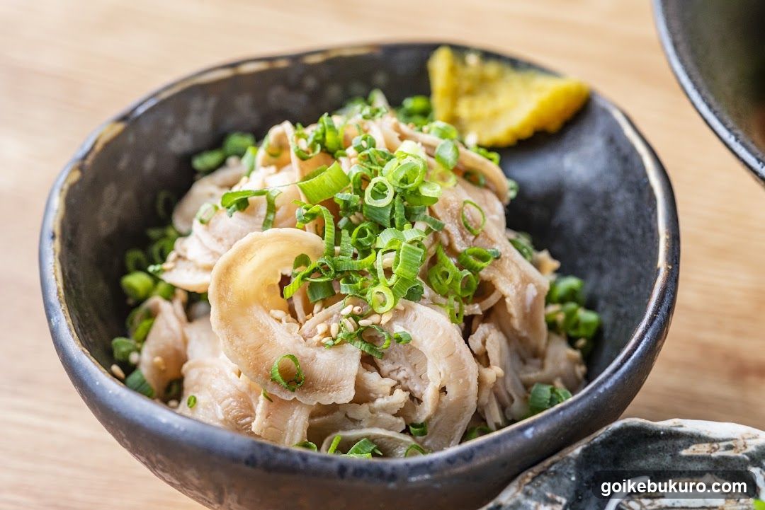 Bowl of sliced meat with green onions and lemon wedge