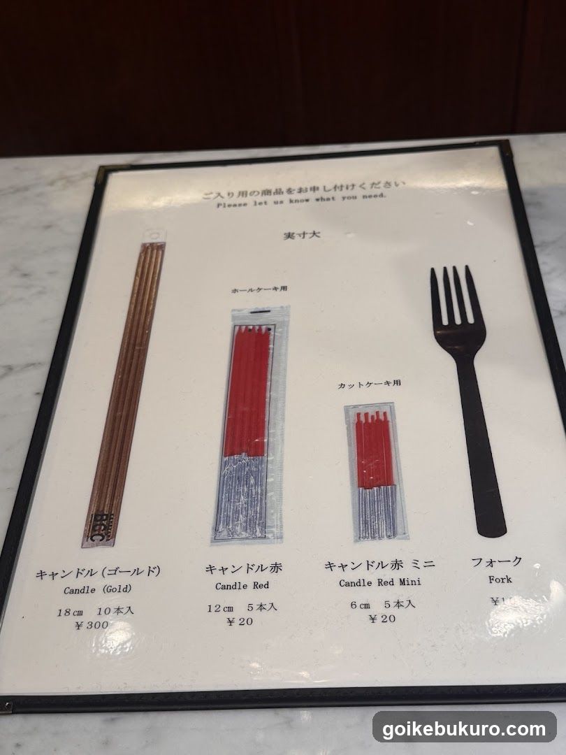 A framed menu board displaying three types of candles and a fork, with prices in yen.