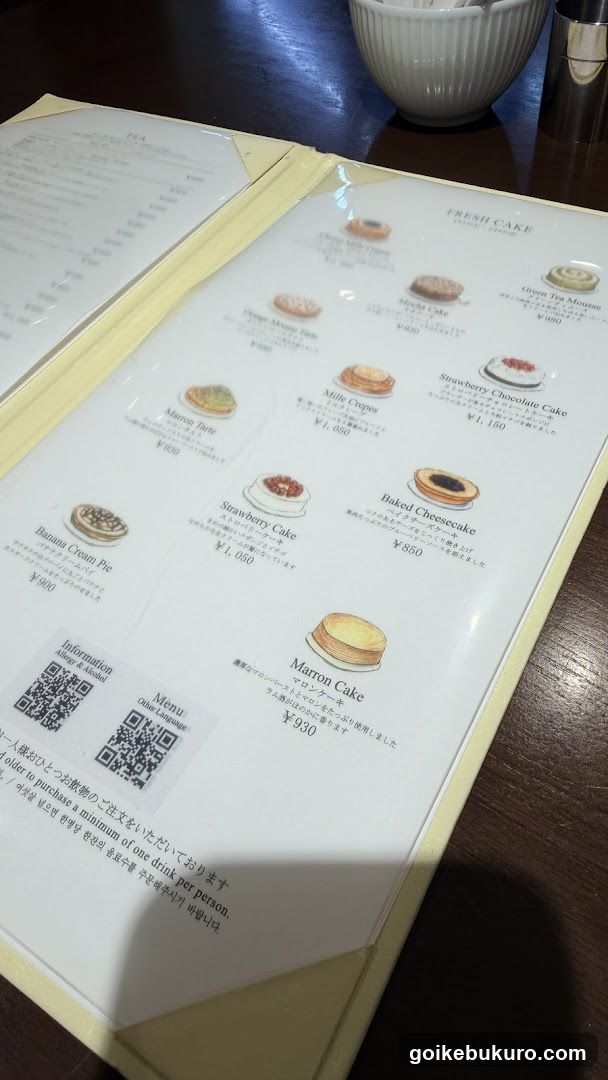 A close-up of a menu page featuring various cake items with prices in yen, including Strawberry Chocolate Cake, Baked Cheesecake, and Maroon Cake.