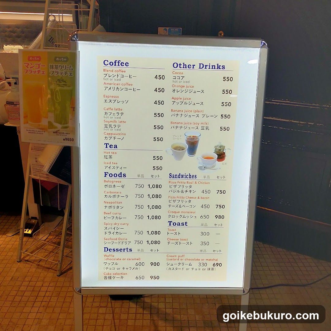 A brightly lit, illuminated menu board displaying coffee, other drinks, sandwiches, toast, desserts, and food items with prices in yen.