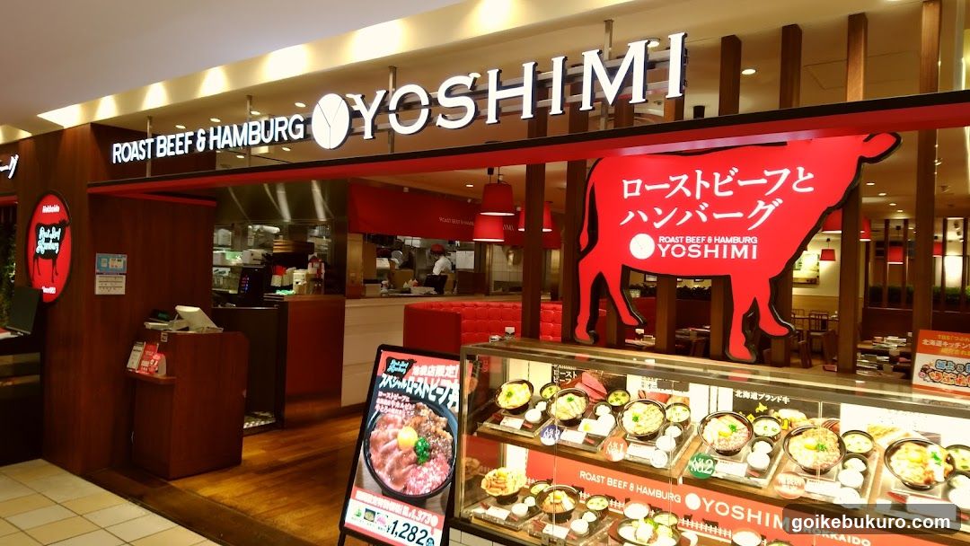 The image shows the storefront of Yoshimi, a restaurant specializing in roast beef and hamburgers. The sign above the entrance reads 'ROAST BEEF & HAMBURG YOSHIMI' with Japanese characters below. A red silhouette of a cow is displayed on the window, along with additional signage featuring the same branding. Inside, there are dining tables and chairs visible through the glass windows.