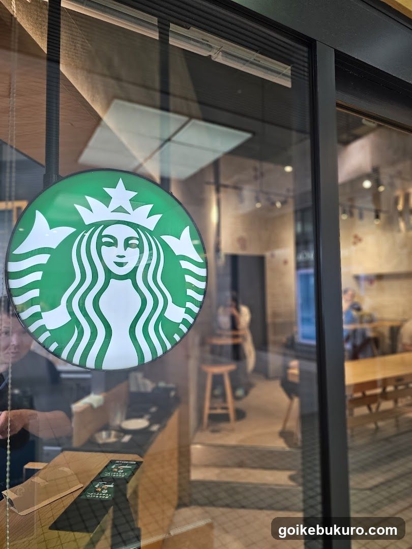 A photo of a Starbucks store entrance, showing the iconic green circular logo with the siren on the glass door. Inside, wooden tables and stools are visible, along with staff members working behind the counter. The interior has warm lighting and modern decor.