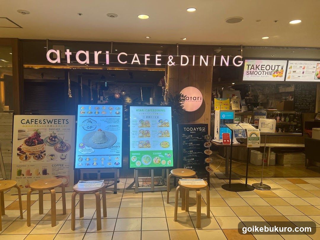 Storefront of atari CAFE & DINING with illuminated signage, menu boards displaying pancakes and desserts, stools outside, and a takeout smoothie sign.