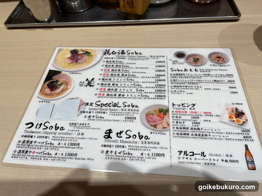 A printed menu featuring various soba noodle dishes, including Tsukemen, Niboshi Mazaesoba, and Soba O-tomi, with prices listed in yen.