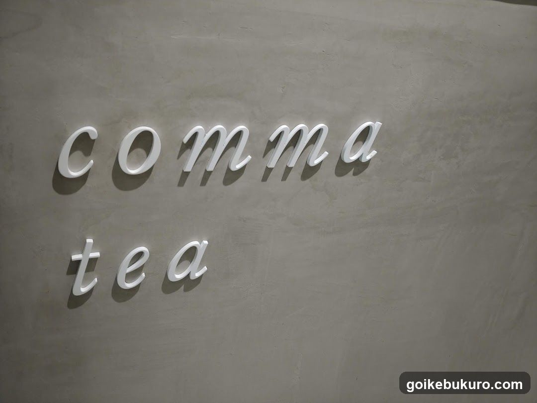 A close-up photo of a textured gray wall with white 3D lettering spelling 'comma' and 'tea', likely part of a shop front or interior signage.