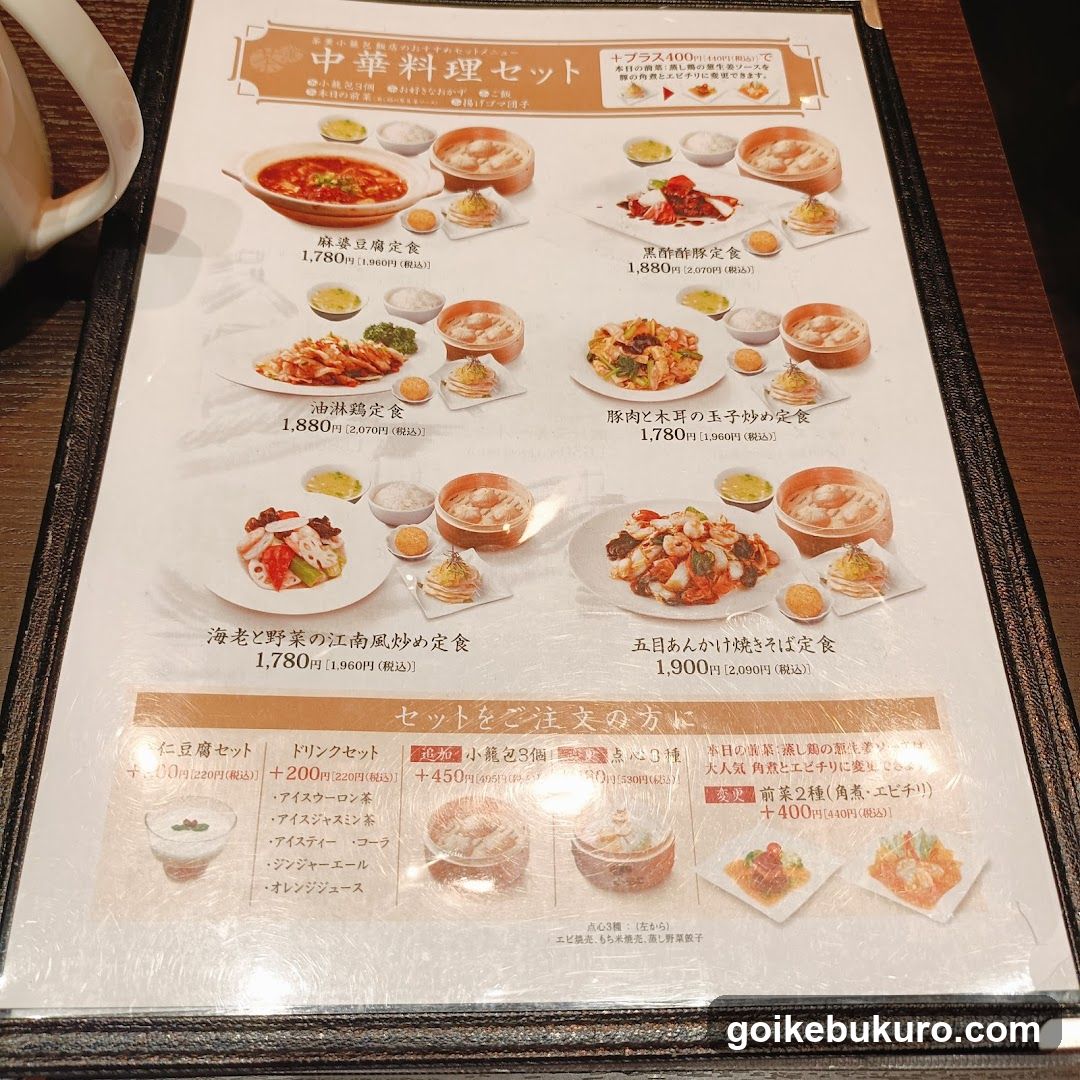 A printed menu showcasing various Chinese dishes with prices in yen, including sets like 'Chinese Cuisine Set' and individual items such as 'Mapo Tofu', 'Black Pepper Shrimp', and 'Pork and Egg Stir-fry'. The menu also lists drink options and additional set combinations.