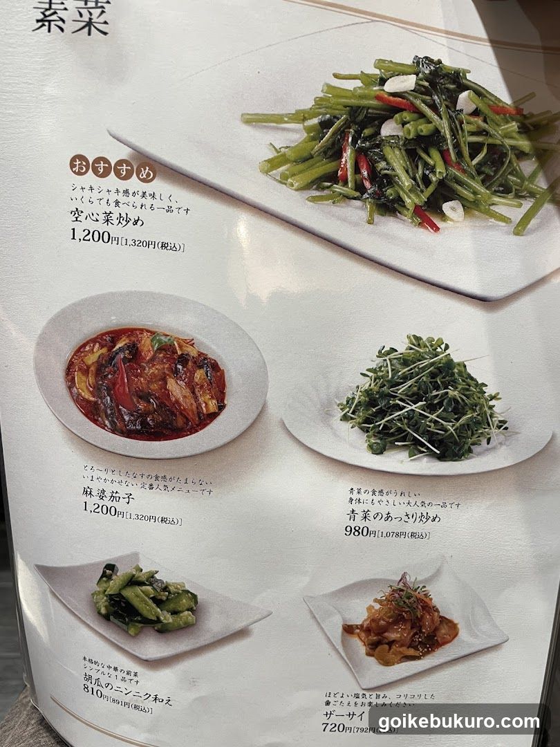 A close-up of a printed menu page featuring four vegetable dishes with Japanese and English descriptions, prices in yen, and an 'Recommended' badge on the top item.