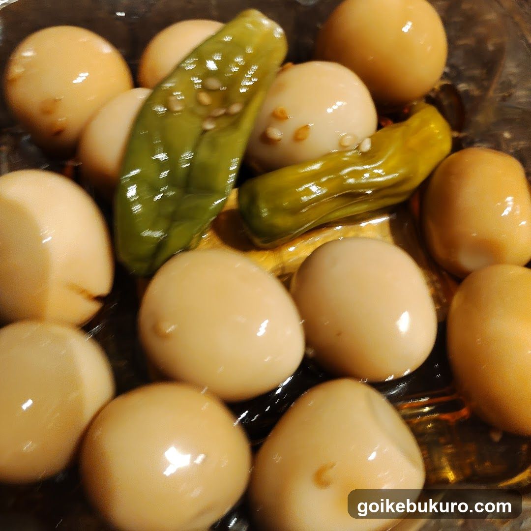 A close-up of glossy, brown-braised eggs in a dark sauce, accompanied by whole green pickled peppers and sesame seeds.